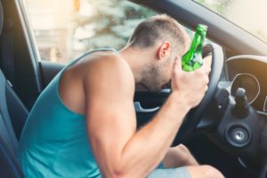 drunk driver holding a bottle behind the steering wheel