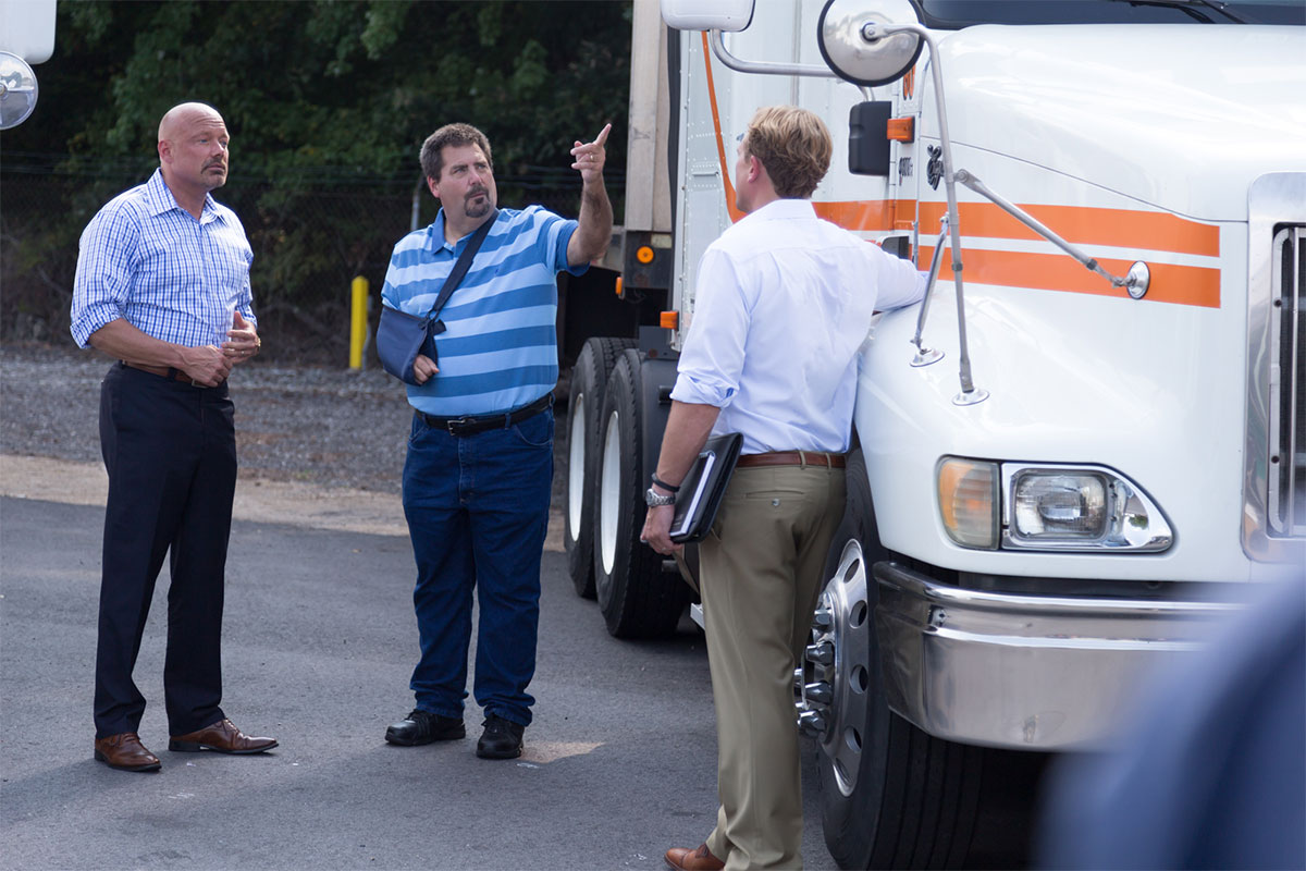 Hombre con el brazo enyesado apuntando a un camión y hablando con dos hombres