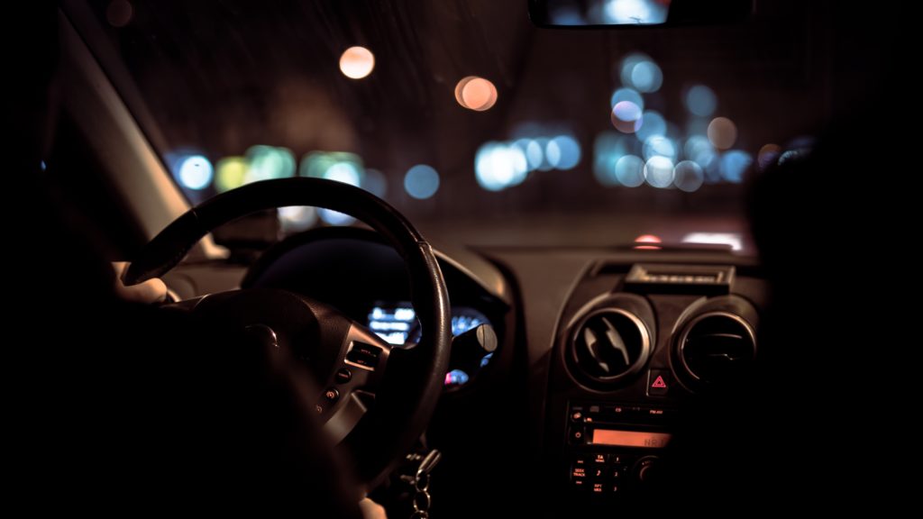 Car steering wheel with windshield showing night sky and blurred car lights
