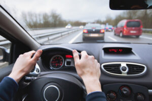 Driver holding a steering wheel while driving on a busy highway.