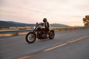 Person driving motorcycle on highway with mountains in background