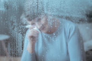 Mujer llorando en un hogar de ancianos, visto a través de una ventana lluviosa