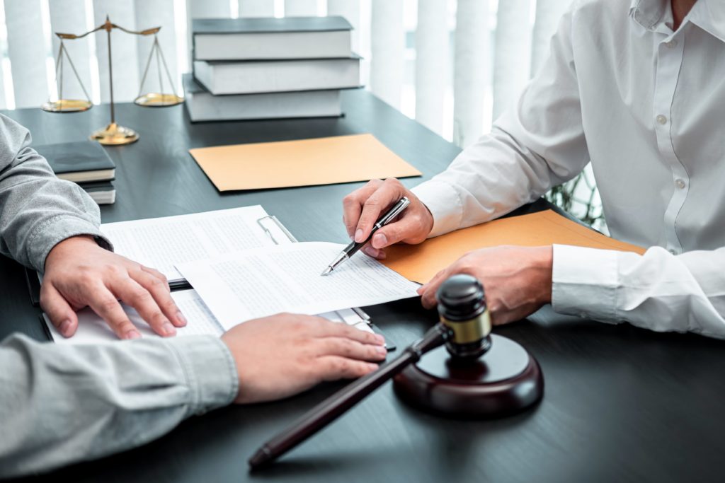 Attorney reviewing legal documents with client at office desk, with gavel and scales of justice in background. Attorney reviewing legal documents with client at office desk, with gavel and scales of justice in background.