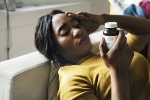 mujer negra, con, dolor de cabeza, lectura, botella de la medicina