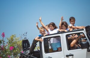 a group of children waving from a moving, open Jeep