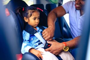 young girl getting buckled into her car seat by her father