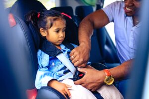 niña siendo abrochada en su asiento de auto por su padre