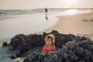 young girl sitting on the sea shore in a sand hole