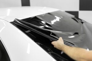 Persona aplicando una lámina tintada oscura en la ventanilla de un coche.