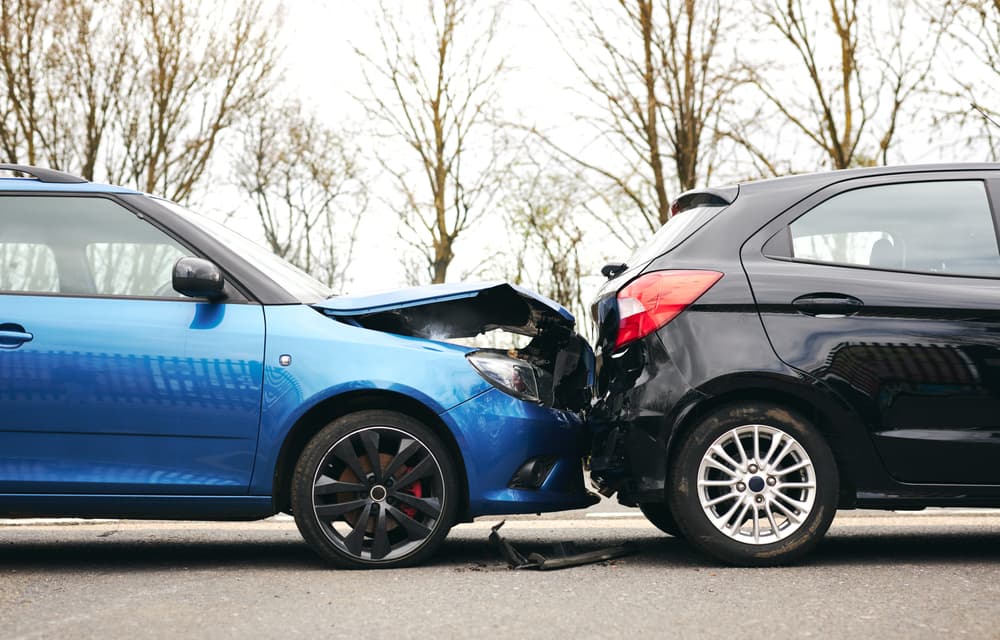 Rear-end car accident with blue vehicle crashing into black car on the road. Rear-end car accident with blue vehicle crashing into black car on the road.