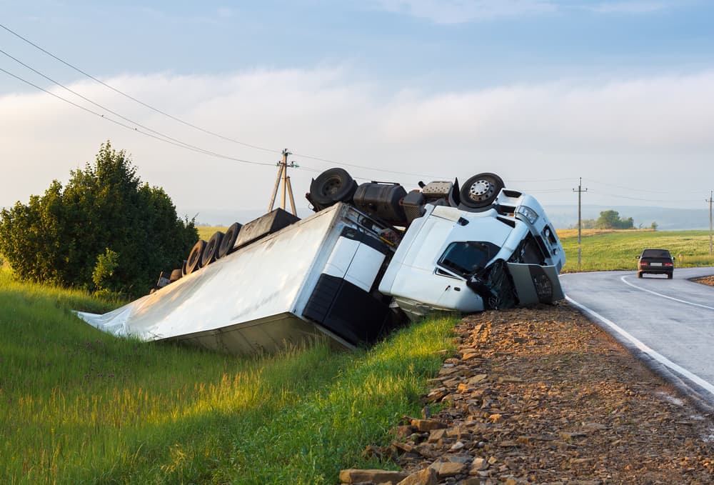 Overturned semi-truck accident on rural road with trailer lying in ditch.