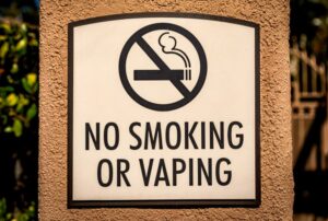 Esta imagen es de un letrero que dice "Prohibido fumar ni vapear", capturada directamente desde el frente para mostrar claramente su diseño y mensaje.