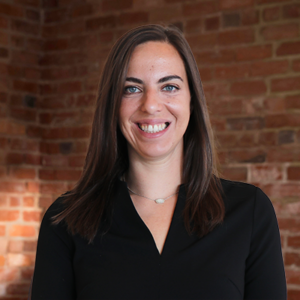 Lawyer Tara, a professional woman with a warm smile, standing in a bright office environment, dressed in a tailored suit.