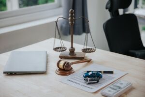Scales of justice, gavel, contract papers, toy car, and money on a desk.