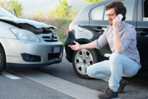 Man on phone inspecting a car accident with front-end damage.