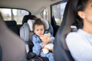 Niña sosteniendo un osito de peluche en un asiento de coche