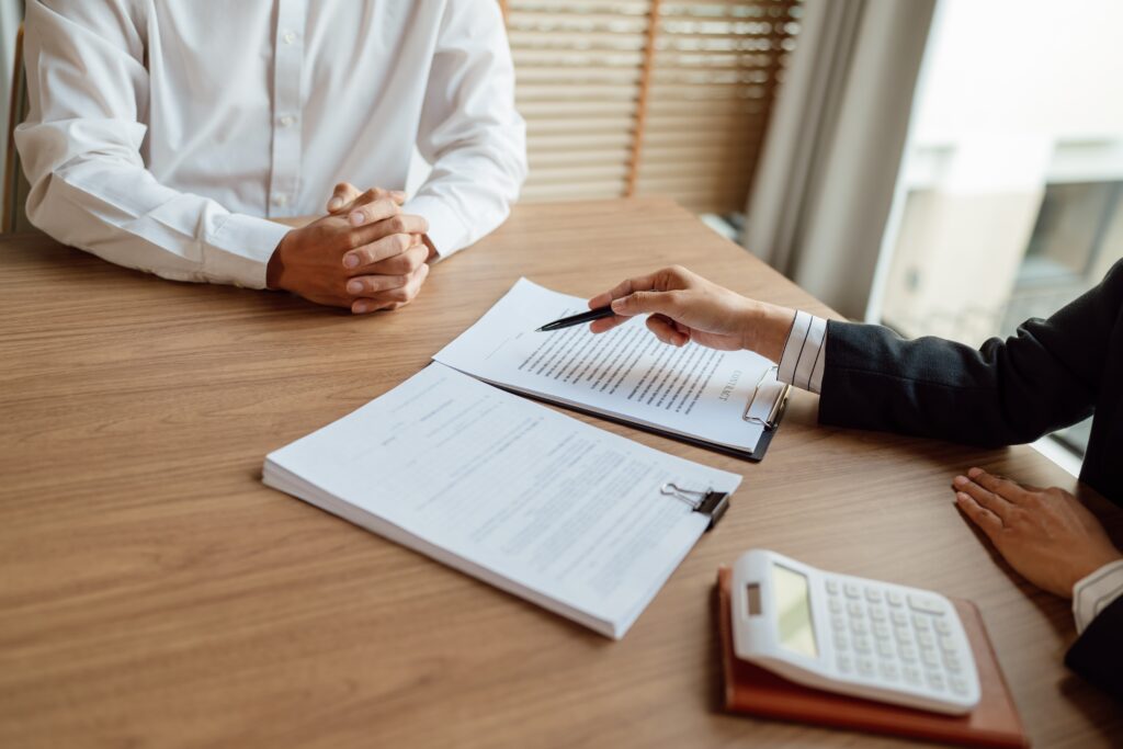 Un abogado revisa documentos legales con un cliente durante una consulta en un escritorio de oficina, con papeles y una calculadora.