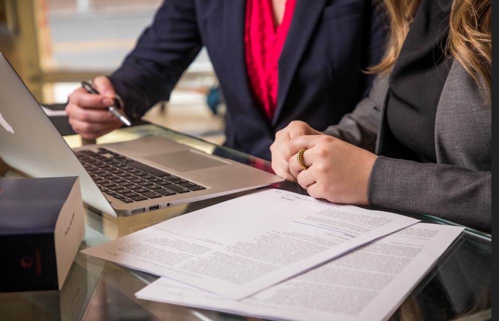 Un abogado revisa documentos legales con un cliente en un escritorio, utilizando una computadora portátil, durante una consulta legal.