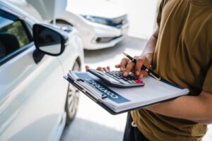Person holding a clipboard and calculator while standing near parked cars.
