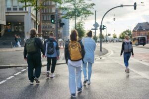 Back view, people on green traffic light cross road at pedestrian crossing