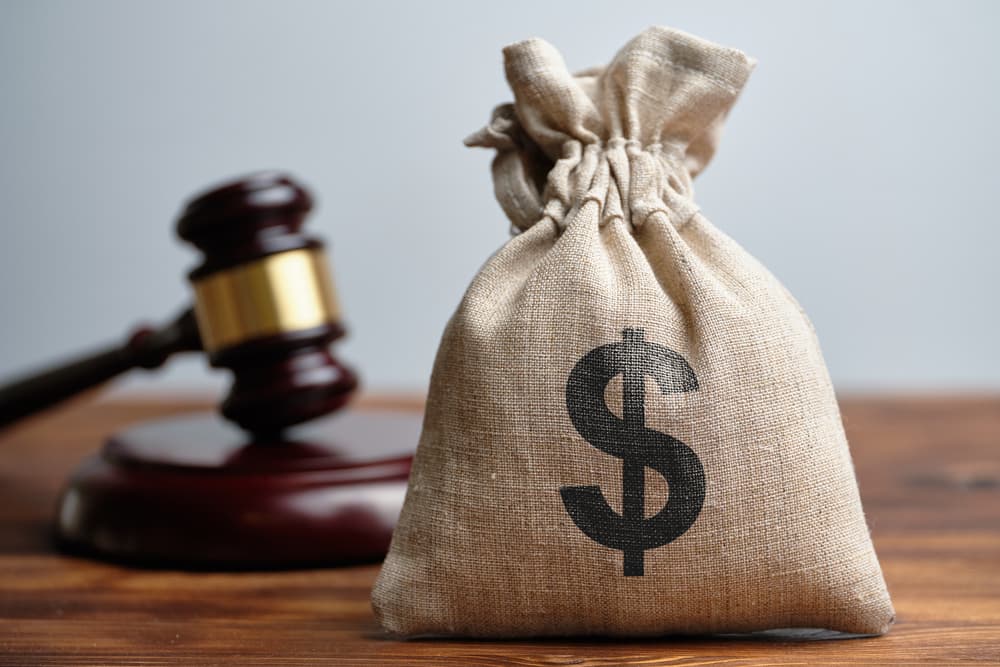 A dollar bag and Judge's gavel in background A dollar bag and Judge's gavel in background