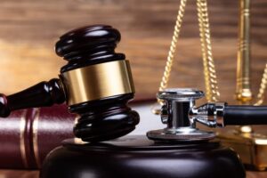 Close-up Of Stethoscope And Gavel In Front Justice Scale On Wooden Desk