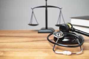 Gavel and stethoscope on a wooden desk with scales of justice in the background.