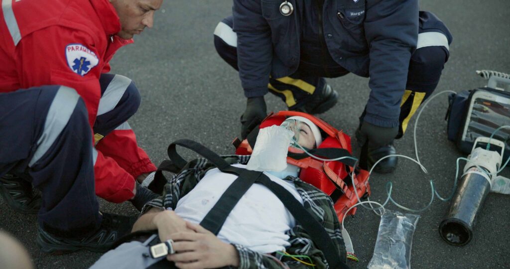 Paramedics providing emergency medical care to injured man after serious accident on road.