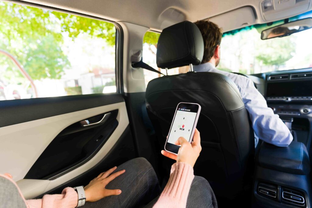 Pasajero utilizando una aplicación de transporte compartido en su teléfono inteligente en el asiento trasero del automóvil, lo que ilustra el servicio de transporte compartido Uber o Lyft.