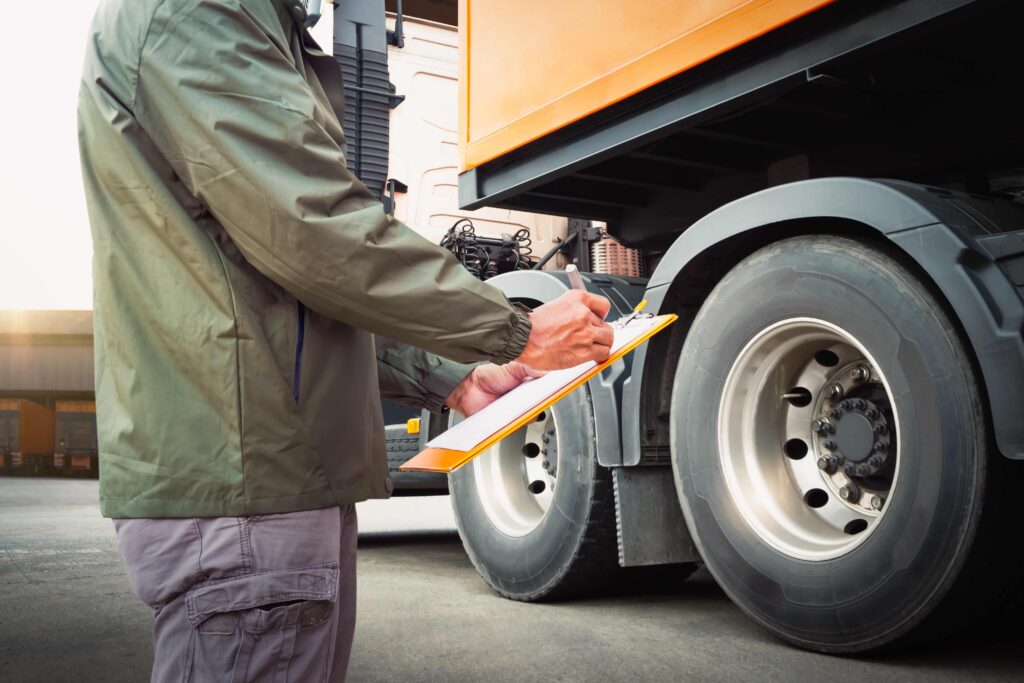 Un camionero realiza una inspección previa al viaje y completa una lista de verificación junto a las ruedas del semirremolque, lo que representa la seguridad de los vehículos comerciales y el cumplimiento de las normas del Departamento de Transporte (DOT). Un camionero realiza una inspección previa al viaje y completa una lista de verificación junto a las ruedas del semirremolque, lo que representa la seguridad de los vehículos comerciales y el cumplimiento de las normas del Departamento de Transporte (DOT).