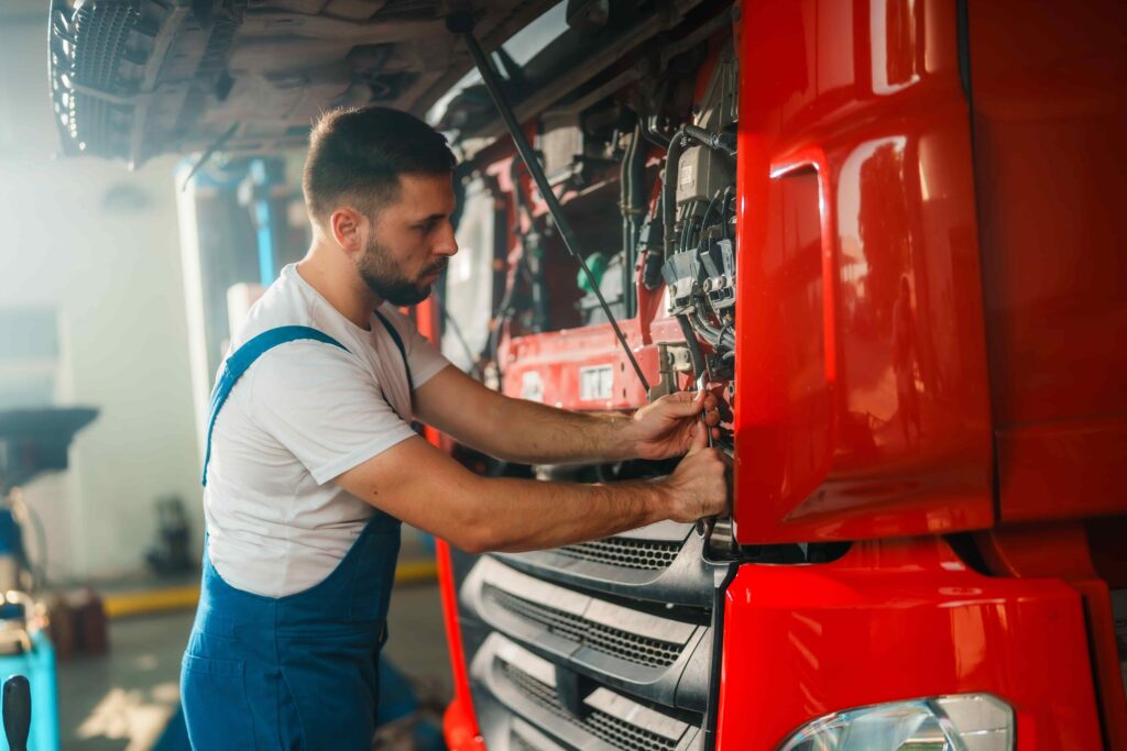 Mecánico de camiones reparando el motor de un semirremolque rojo en un taller, lo que representa el mantenimiento de vehículos comerciales y el trabajo en la industria del transporte por carretera. Mecánico de camiones reparando el motor de un semirremolque rojo en un taller, lo que representa el mantenimiento de vehículos comerciales y el trabajo en la industria del transporte por carretera.
