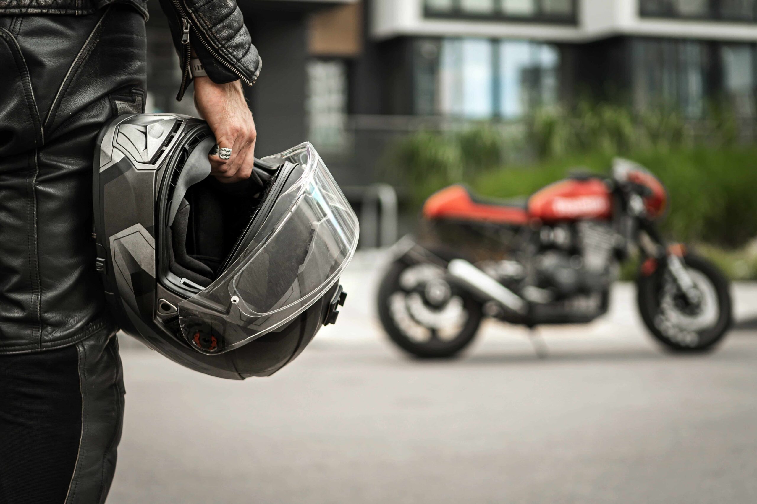 Motociclista sosteniendo un casco junto a su motocicleta en una calle de la ciudad, lo que representa la seguridad vial para motociclistas y el riesgo de accidentes.