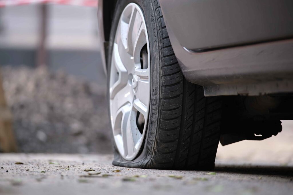 Flat tire on a parked car, showing damaged and deflated tire on roadside pavement. Flat tire on a parked car, showing damaged and deflated tire on roadside pavement.