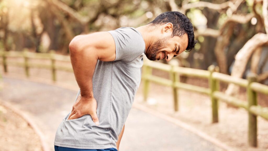 Man holding lower back in pain while standing on outdoor trail, illustrating back injury and personal injury claim concept.