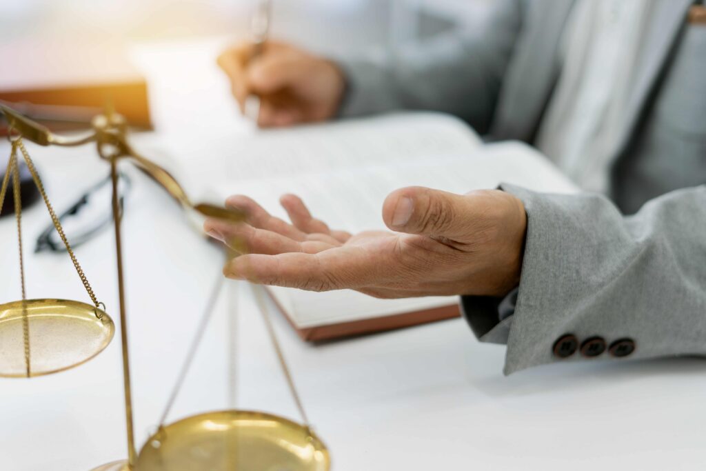 Lawyer explaining legal details with open hand gesture beside scales of justice and documents, representing legal consultation and case discussion.