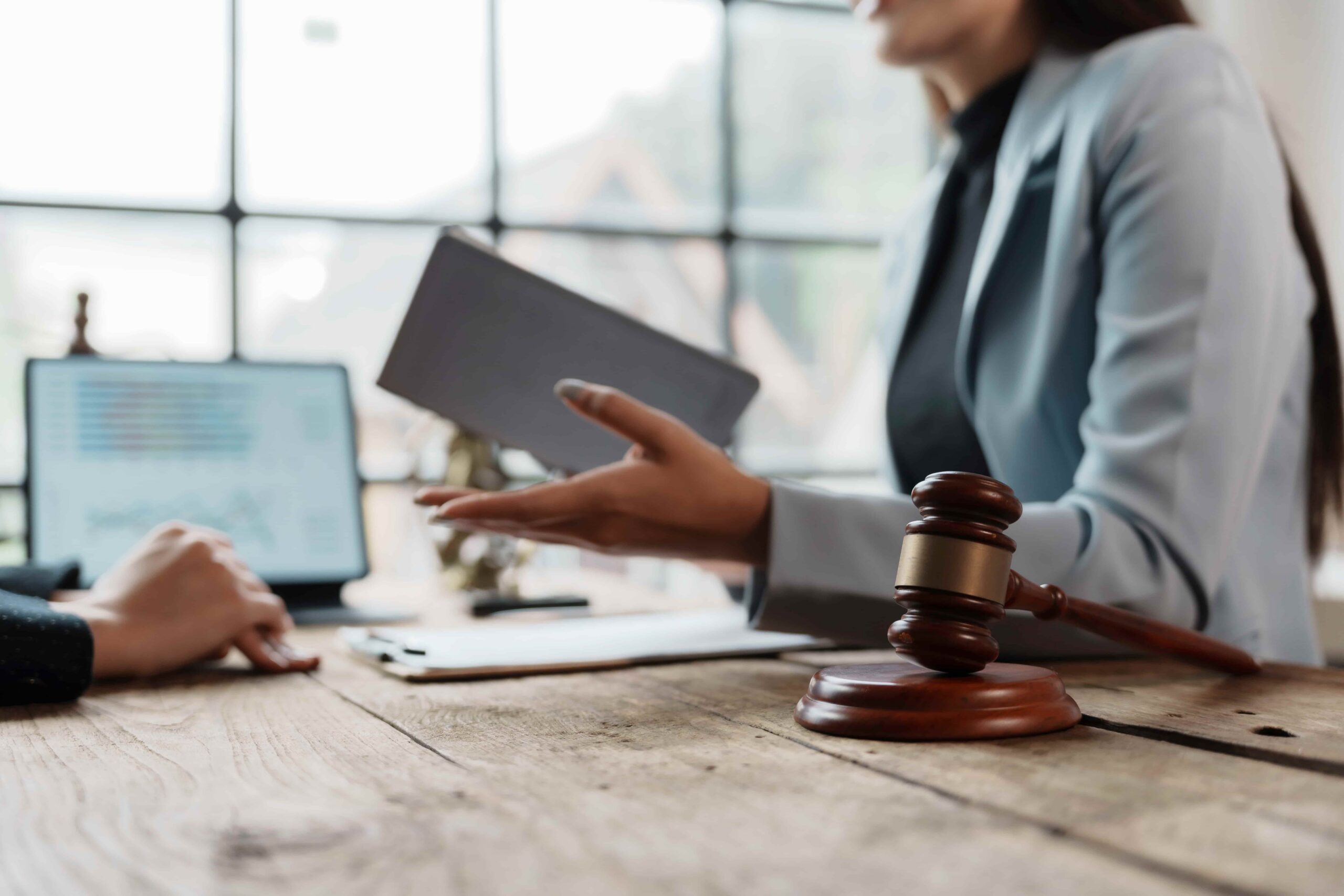 Abogado consultando con un cliente en su escritorio, con mazo y documentos legales, discutiendo la estrategia del caso y brindando asesoramiento legal en un entorno de oficina moderno.