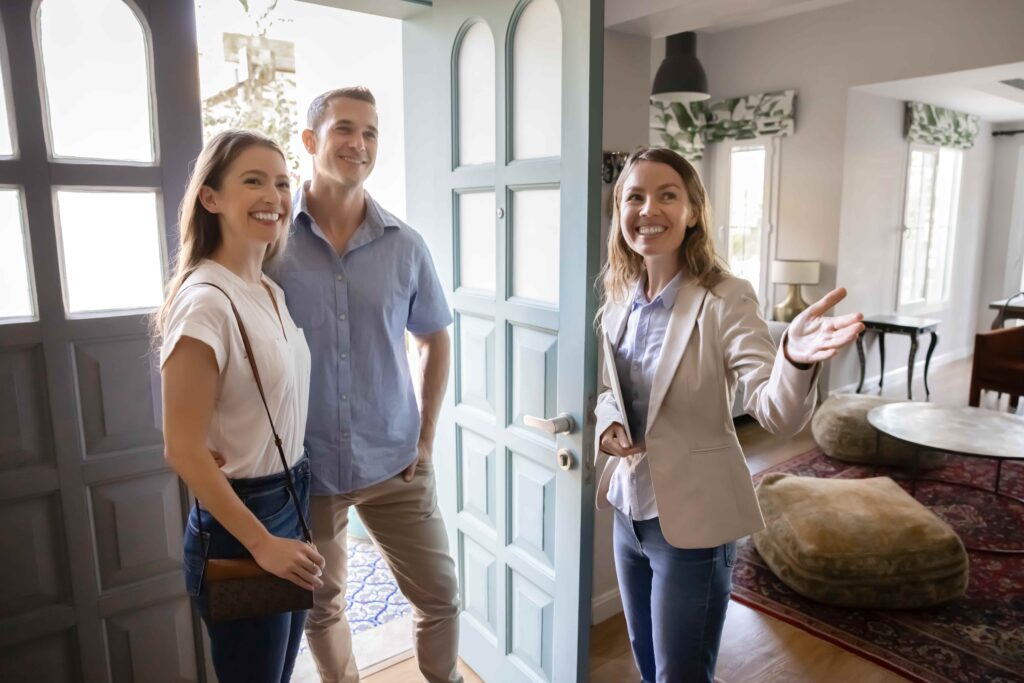 Agente inmobiliario da la bienvenida a una pareja sonriente a su casa, representando la visita a la propiedad, el proceso de compra de una vivienda y los servicios inmobiliarios. Agente inmobiliario da la bienvenida a una pareja sonriente a su casa, representando la visita a la propiedad, el proceso de compra de una vivienda y los servicios inmobiliarios.