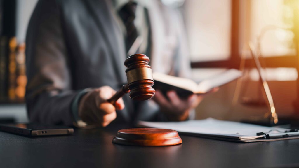 Juez sosteniendo un mazo sobre la caja negra en la sala del tribunal con un libro de leyes, simbolizando la decisión legal, el fallo judicial y el sistema de justicia.