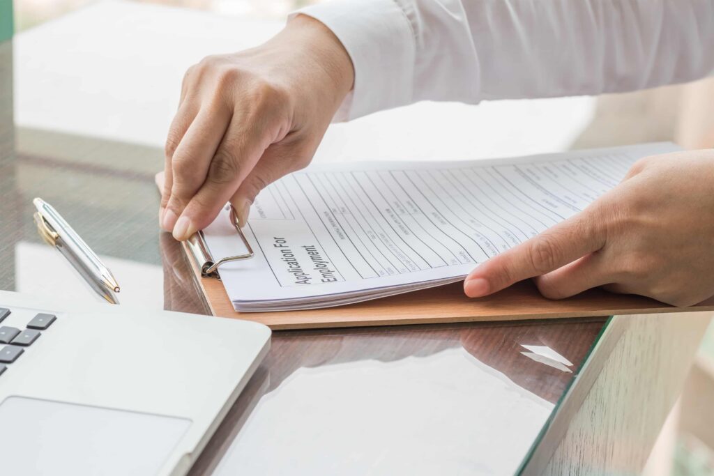 HR professional reviewing and clipping an employment application form on a clipboard next to a laptop, representing hiring process and job application screening.